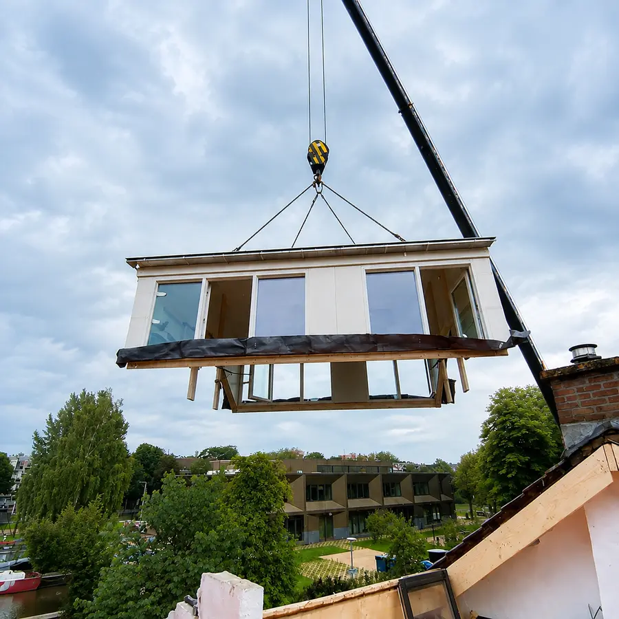 Een prefab dakkapel hangt aan de kraan boven het dak